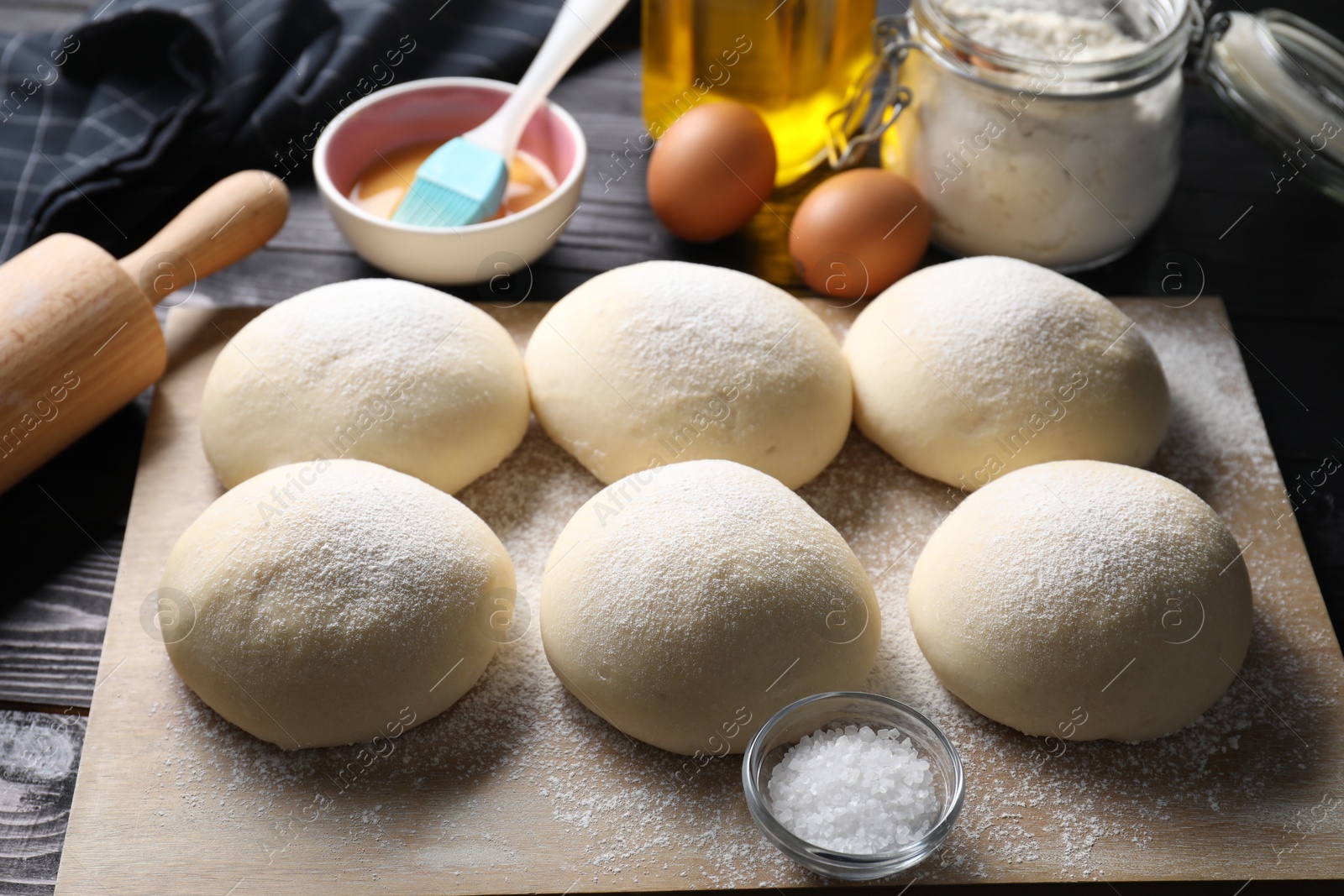 Photo of Raw dough balls, yolk, salt, flour, eggs and rolling pin on black wooden table