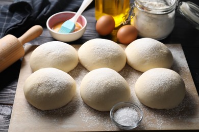 Photo of Raw dough balls, yolk, salt, flour, eggs and rolling pin on black wooden table