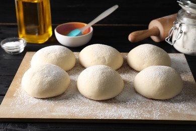 Raw dough balls, yolk, oil, flour, salt and rolling pin on black wooden table