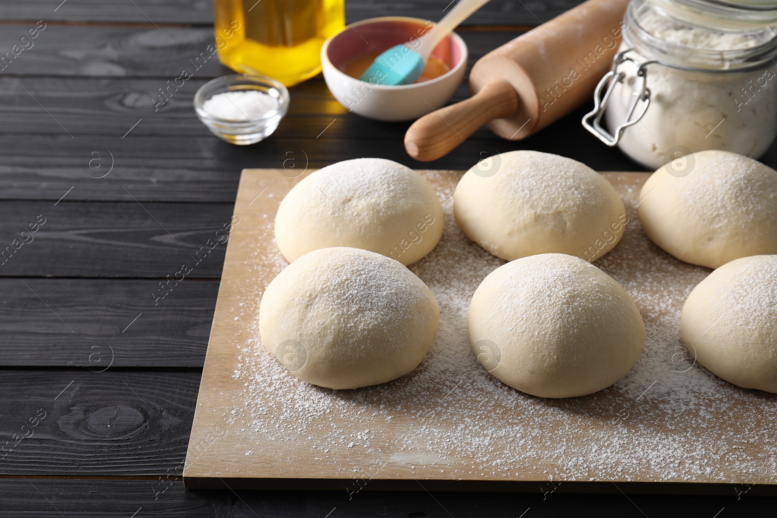 Photo of Raw dough balls, yolk, flour, salt and rolling pin on black wooden table