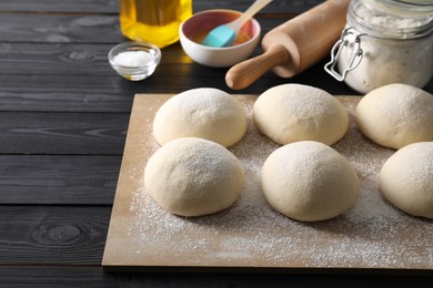 Raw dough balls, yolk, flour, salt and rolling pin on black wooden table