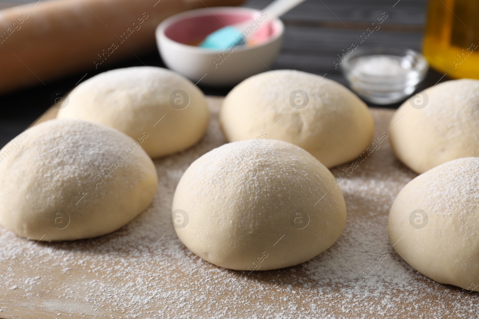 Photo of Raw dough balls and flour on table, closeup