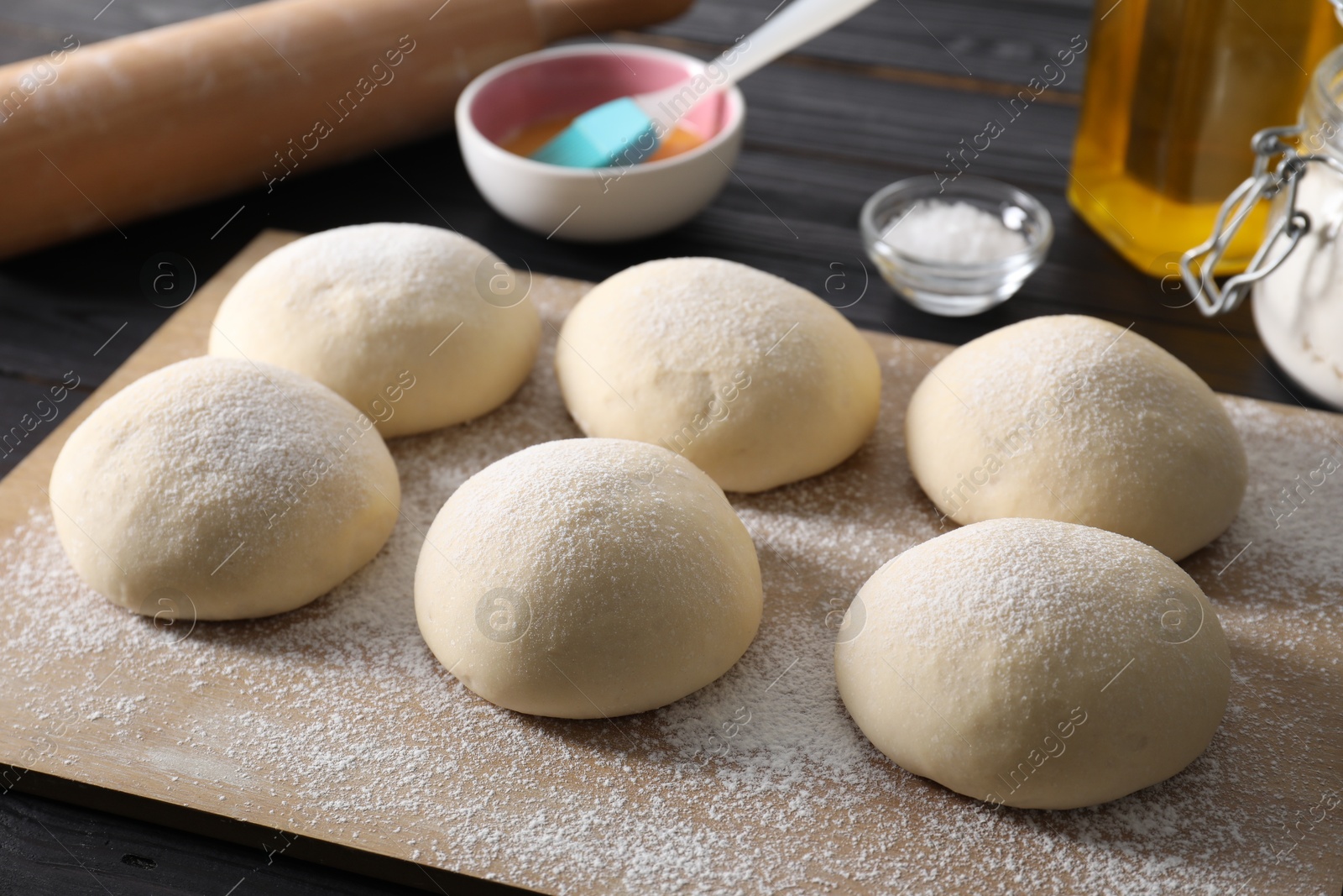 Photo of Raw dough balls, yolk, salt and rolling pin on black wooden table