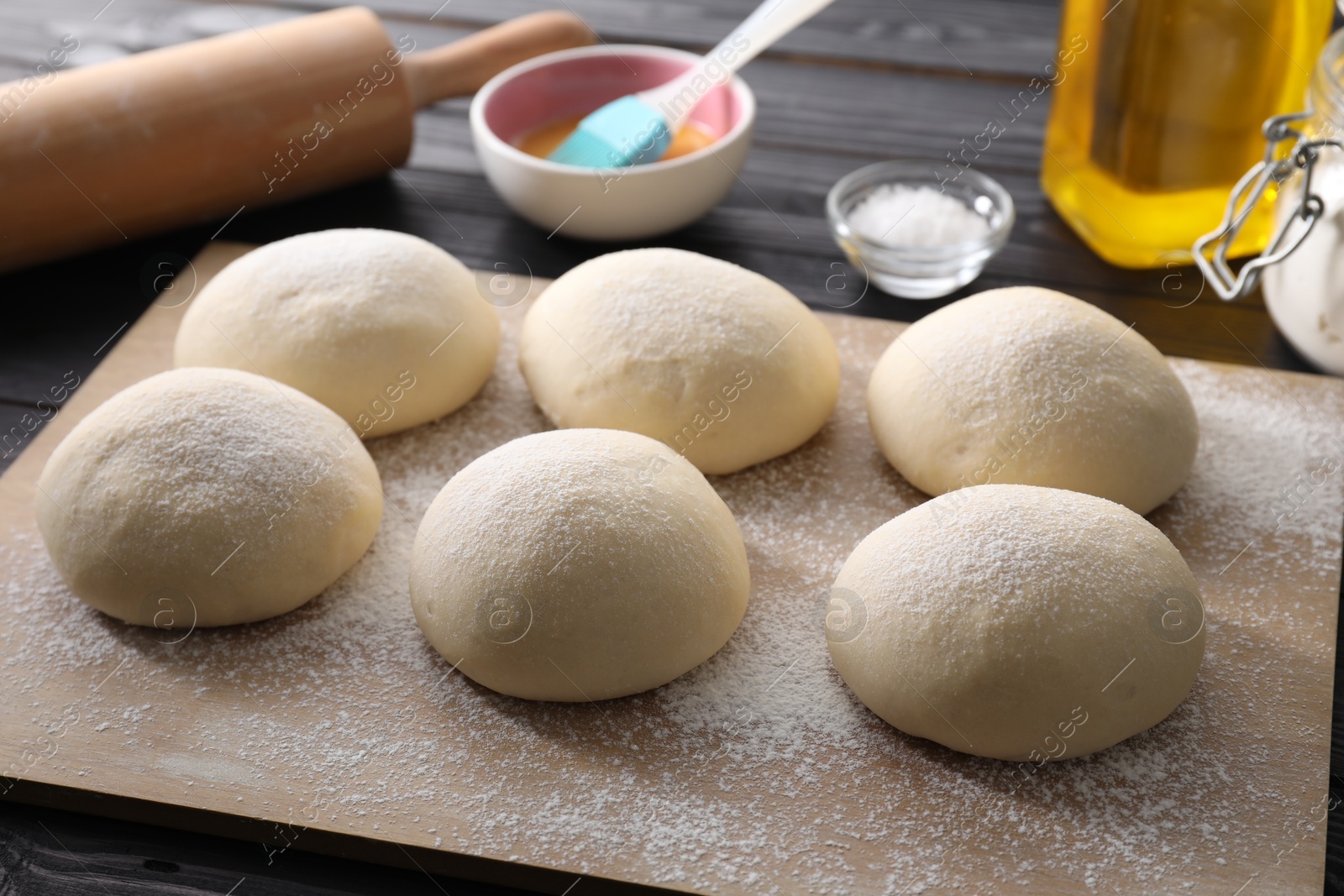 Photo of Raw dough balls, yolk, salt and rolling pin on black wooden table