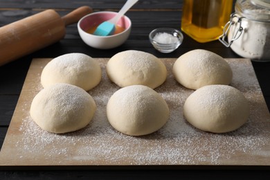 Raw dough balls, yolk, oil, flour, salt and rolling pin on black wooden table