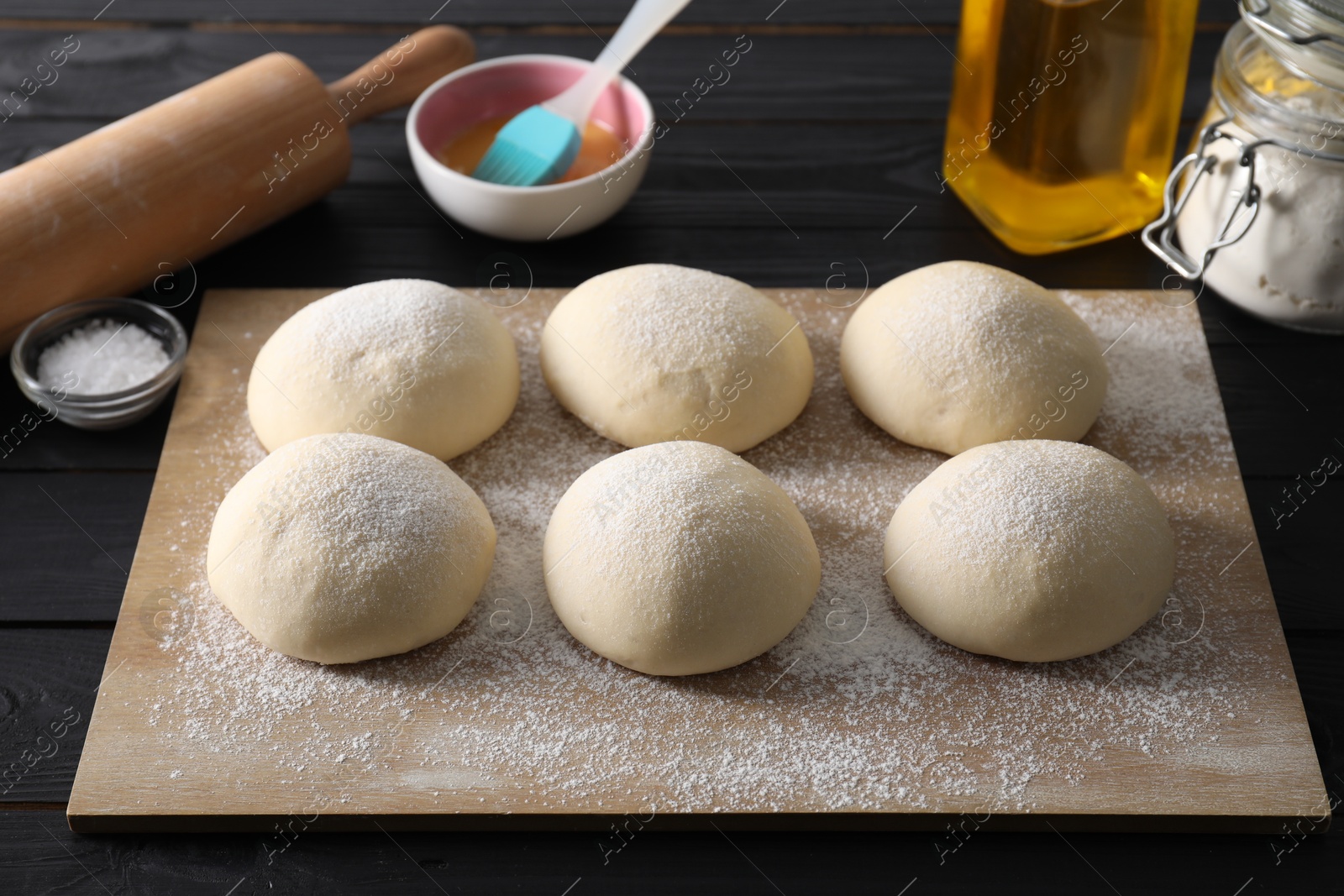 Photo of Raw dough balls, yolk, oil, flour, salt and rolling pin on black wooden table