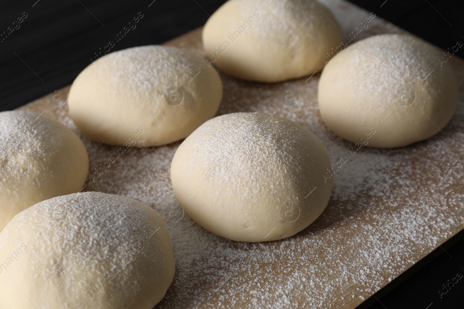 Photo of Raw dough balls with flour on table, closeup