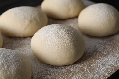 Photo of Raw dough balls with flour on table, closeup