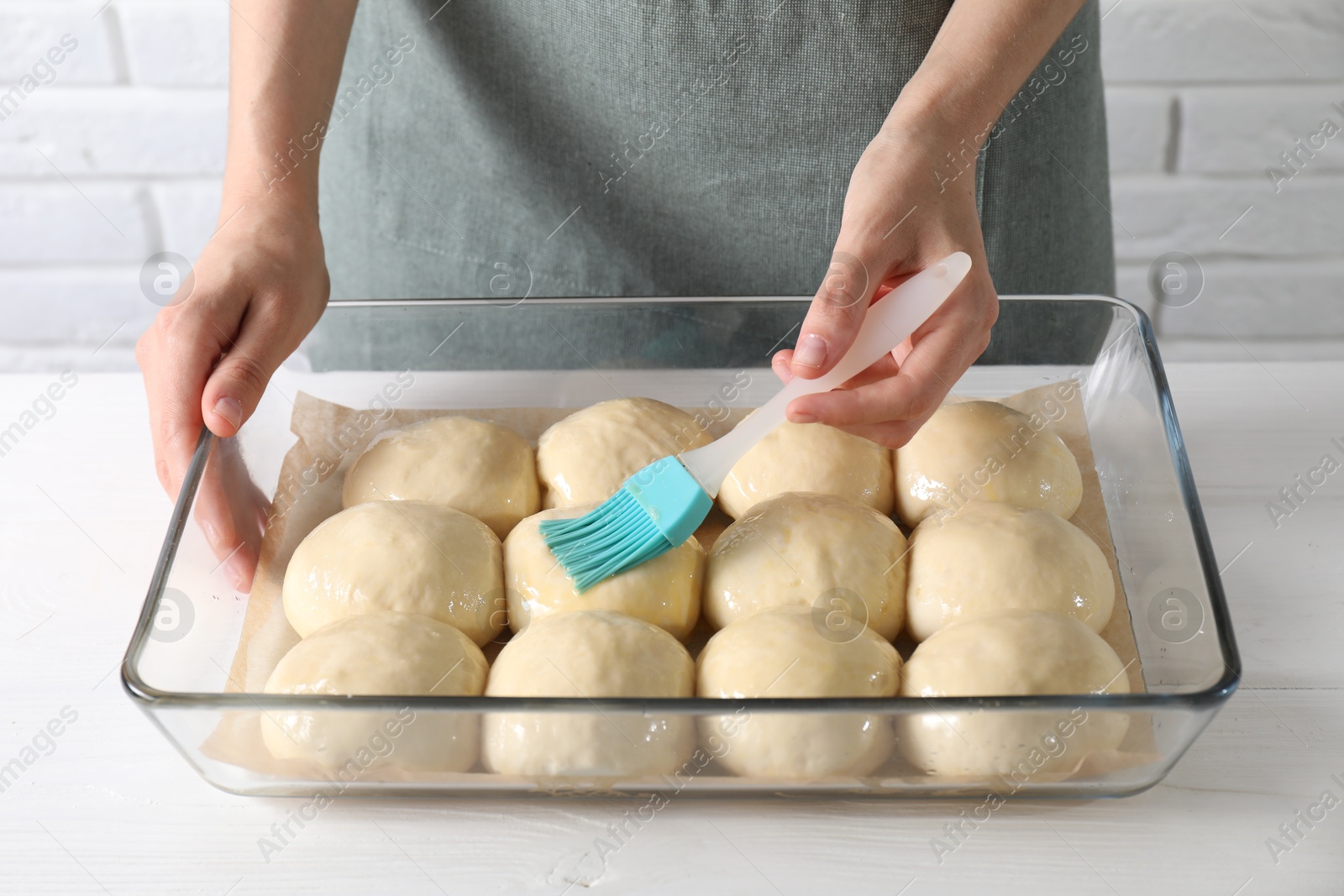 Photo of Woman spreading egg yolk onto raw dough balls at white wooden table, closeup