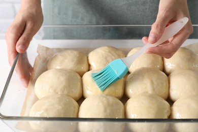 Woman spreading egg yolk onto raw dough balls at table, closeup