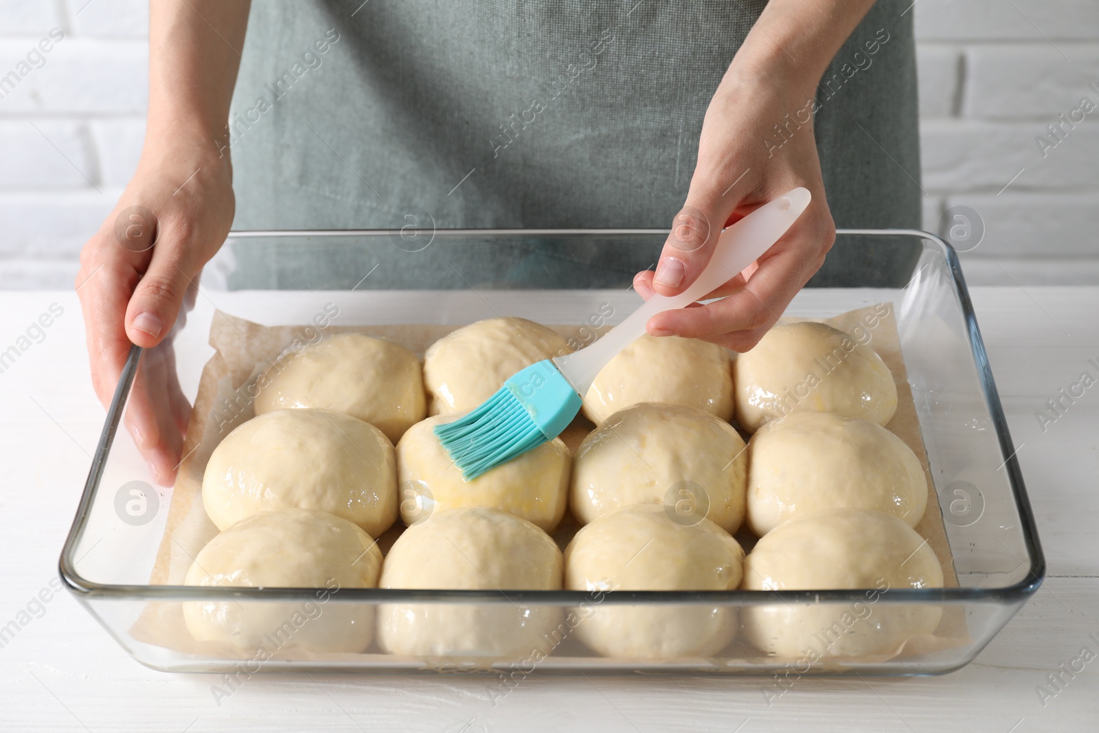 Photo of Woman spreading egg yolk onto raw dough balls at white wooden table, closeup