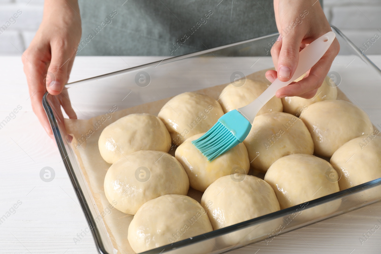 Photo of Woman spreading egg yolk onto raw dough balls at white wooden table, closeup