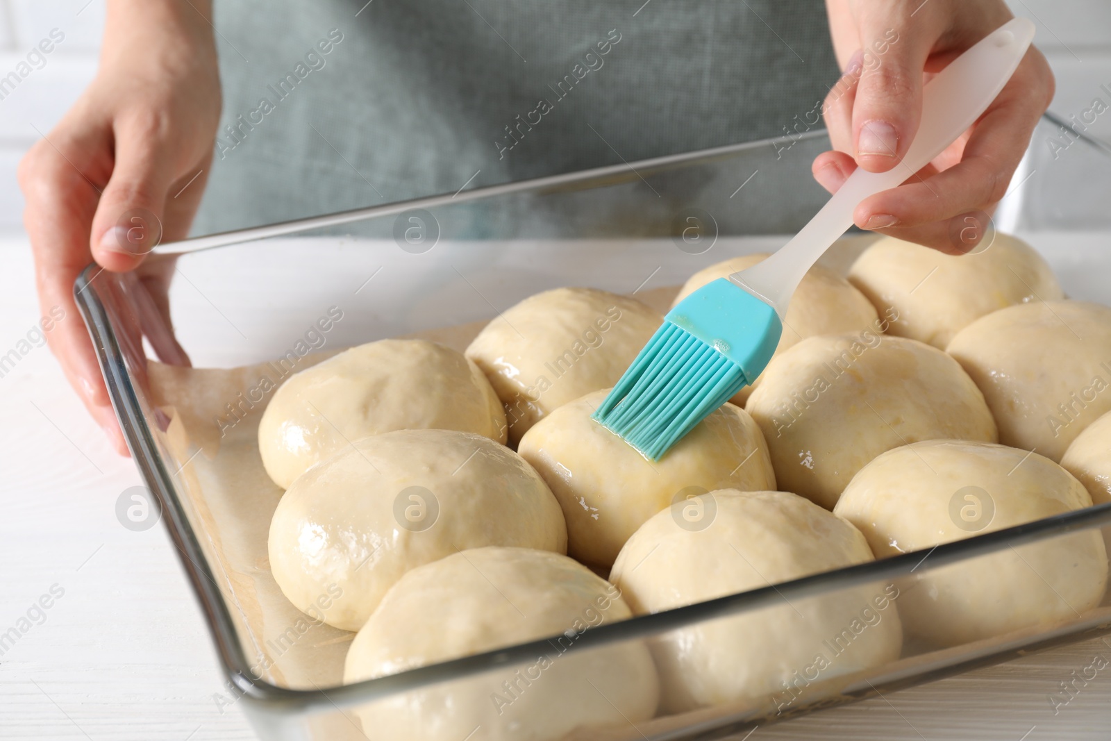 Photo of Woman spreading egg yolk onto raw dough balls at white wooden table, closeup