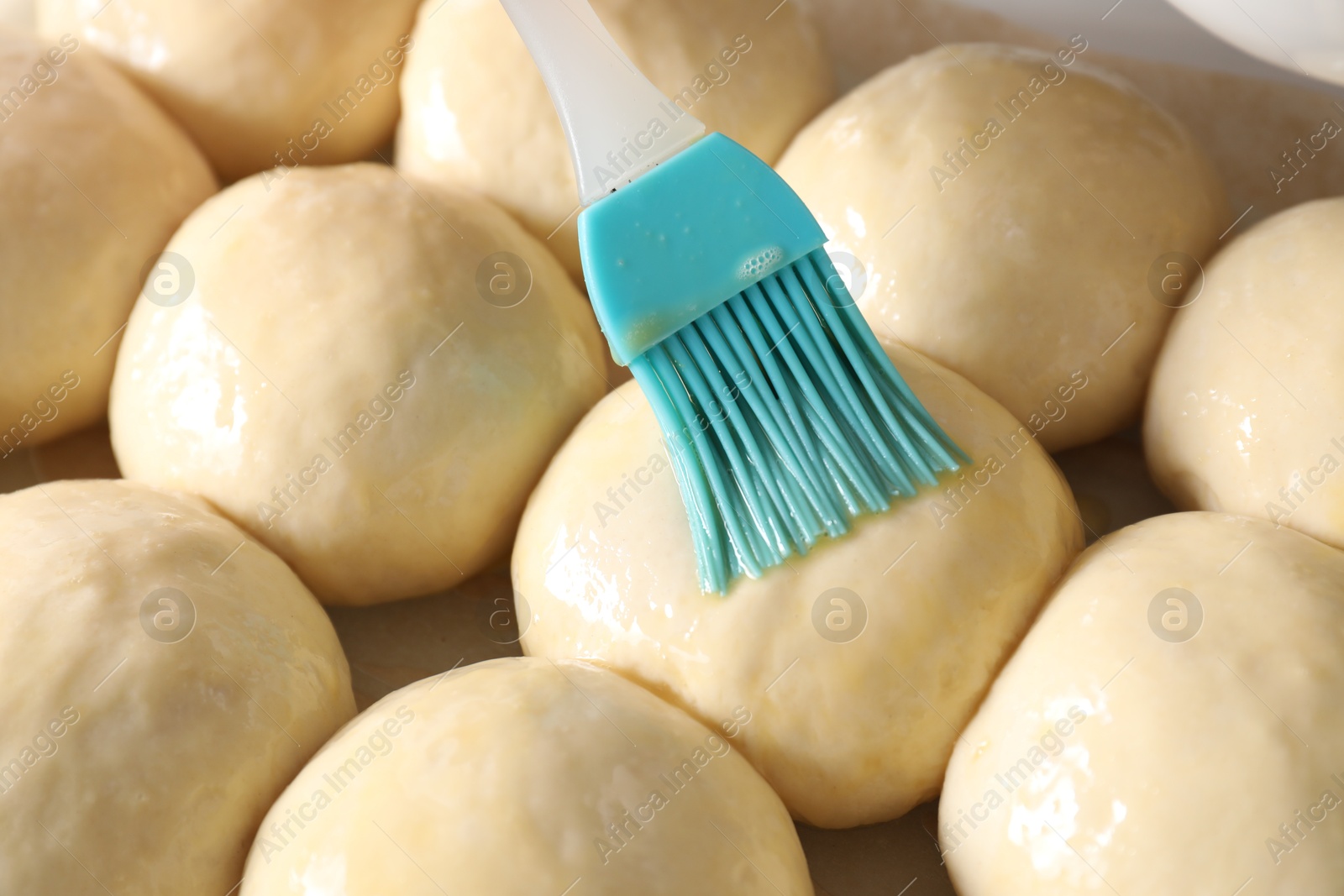 Photo of Spreading egg yolk onto raw dough balls, closeup