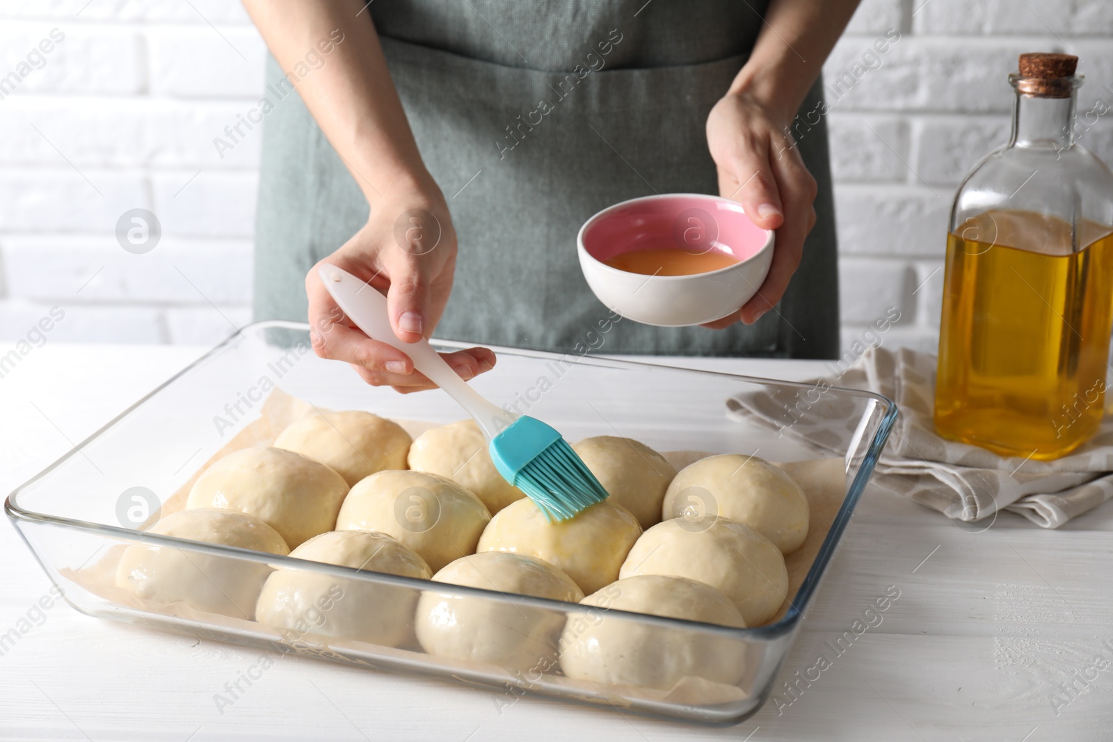 Photo of Woman spreading egg yolk onto raw dough balls at white wooden table, closeup