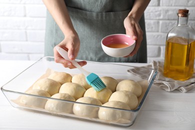 Woman spreading egg yolk onto raw dough balls at white wooden table, closeup