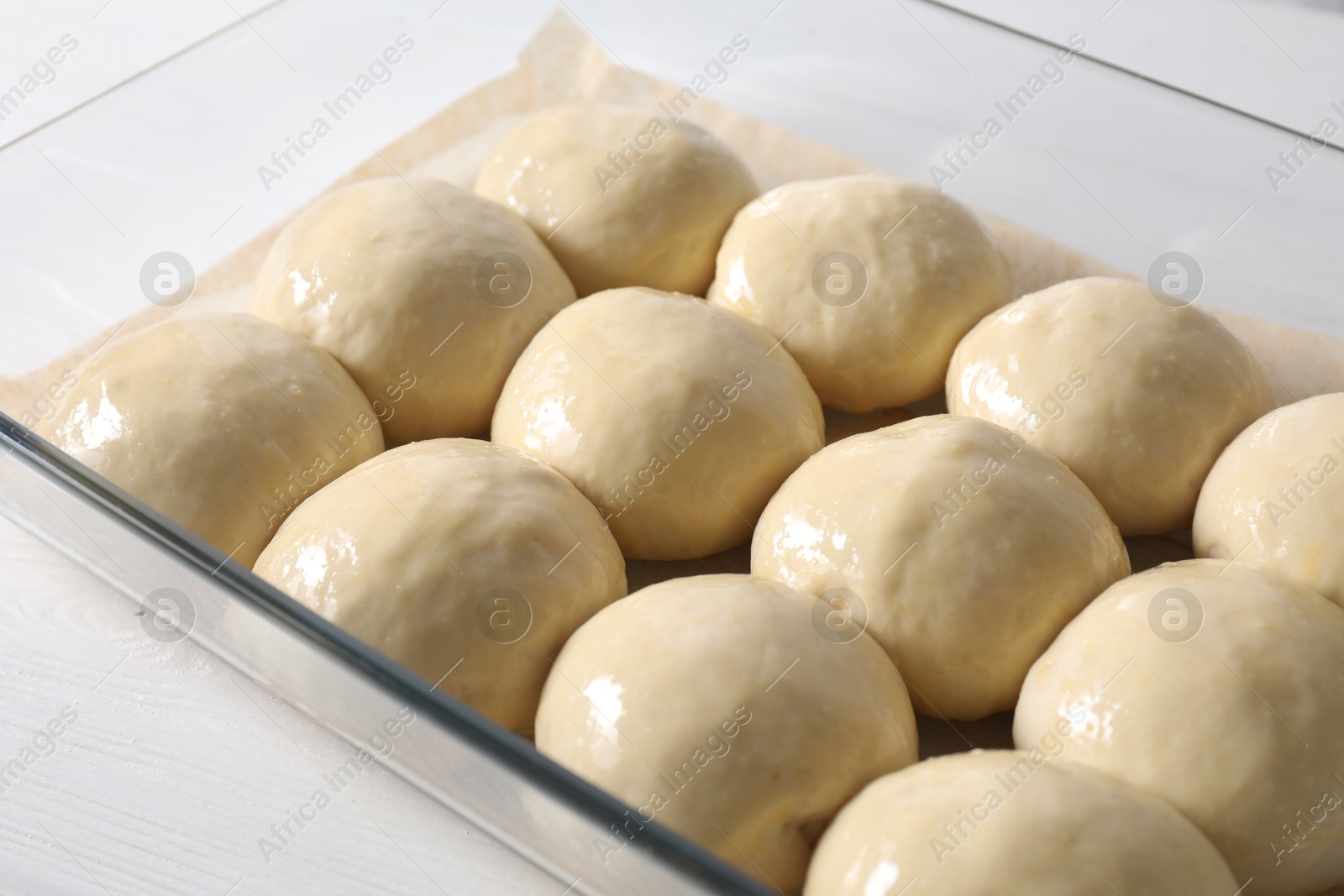 Photo of Raw dough balls in baking dish on white wooden table