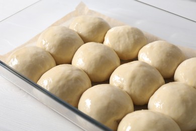 Raw dough balls in baking dish on white wooden table