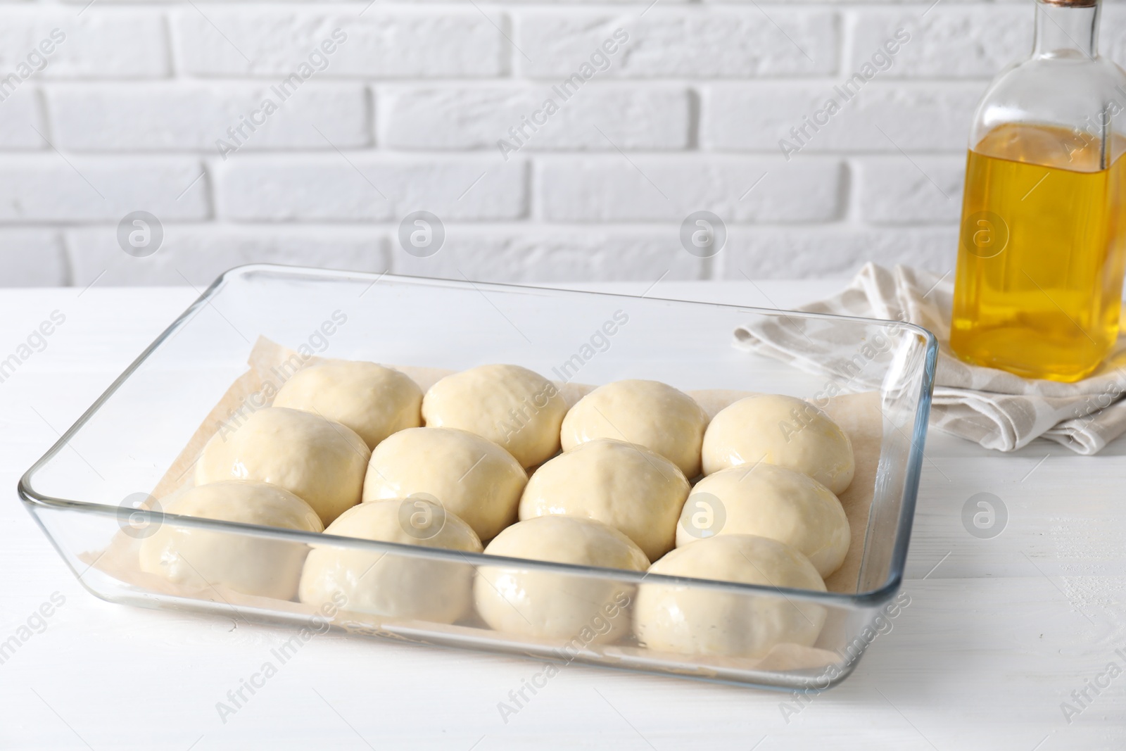 Photo of Raw dough balls in baking dish and oil on white wooden table