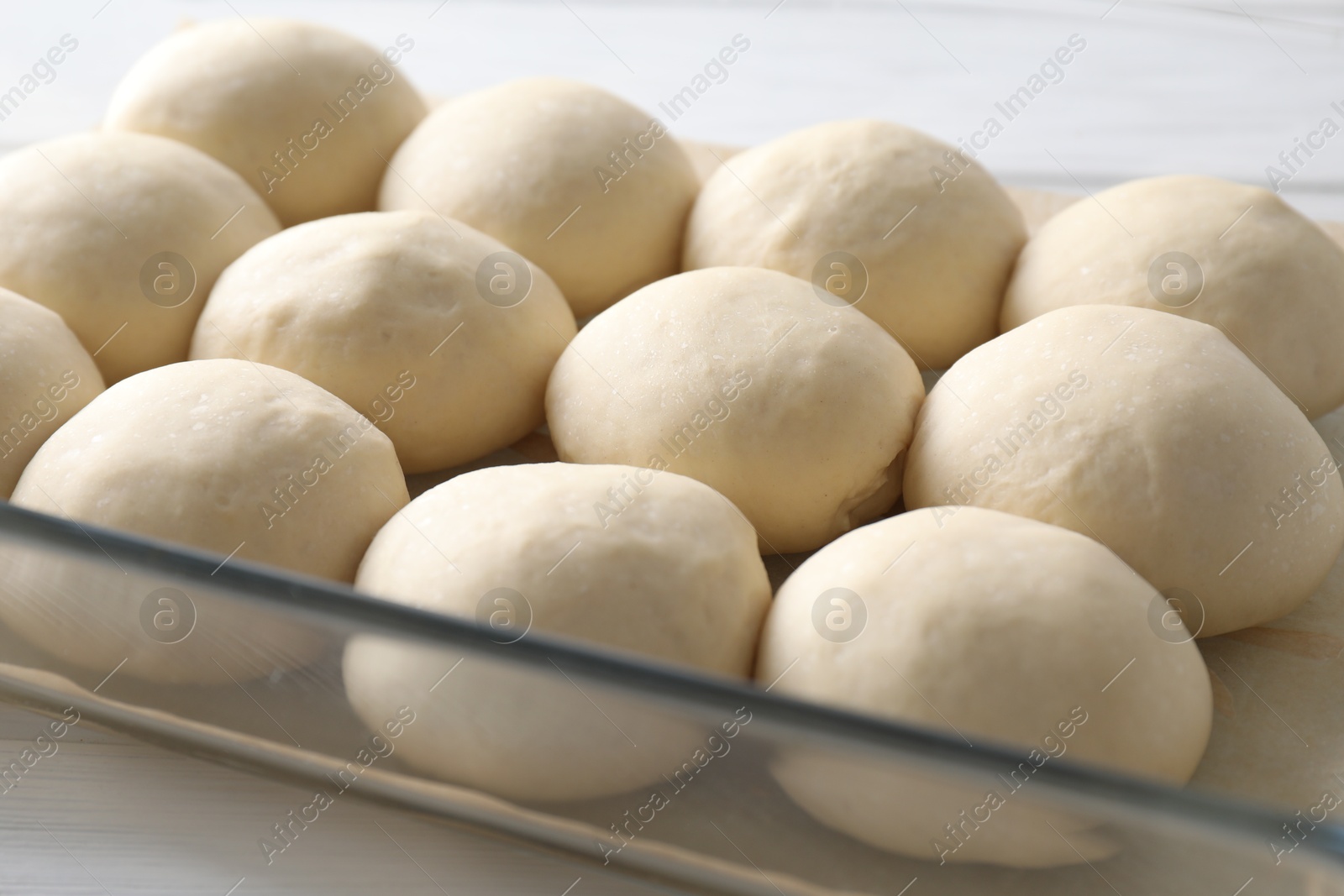 Photo of Raw dough balls in baking dish on white wooden table, closeup