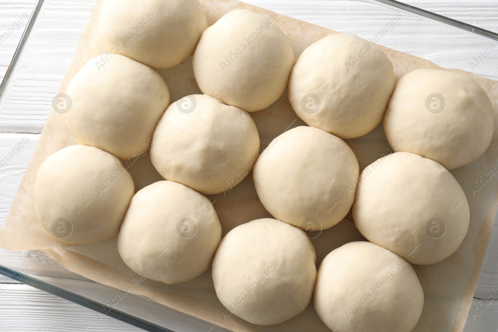 Photo of Raw dough balls in baking dish on white wooden table, top view