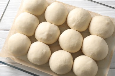 Raw dough balls in baking dish on white wooden table, top view