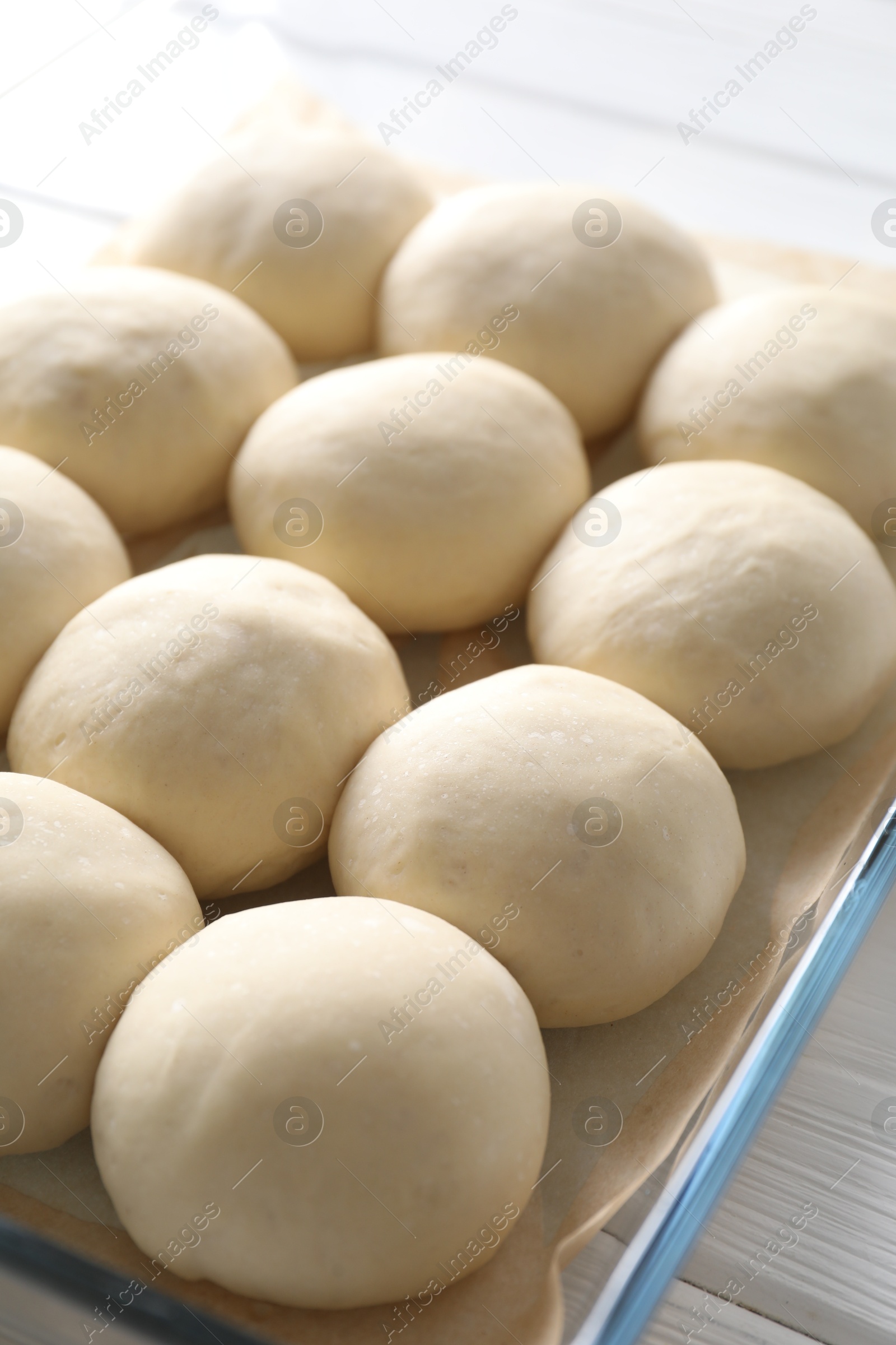 Photo of Raw dough balls in baking dish on white wooden table, closeup