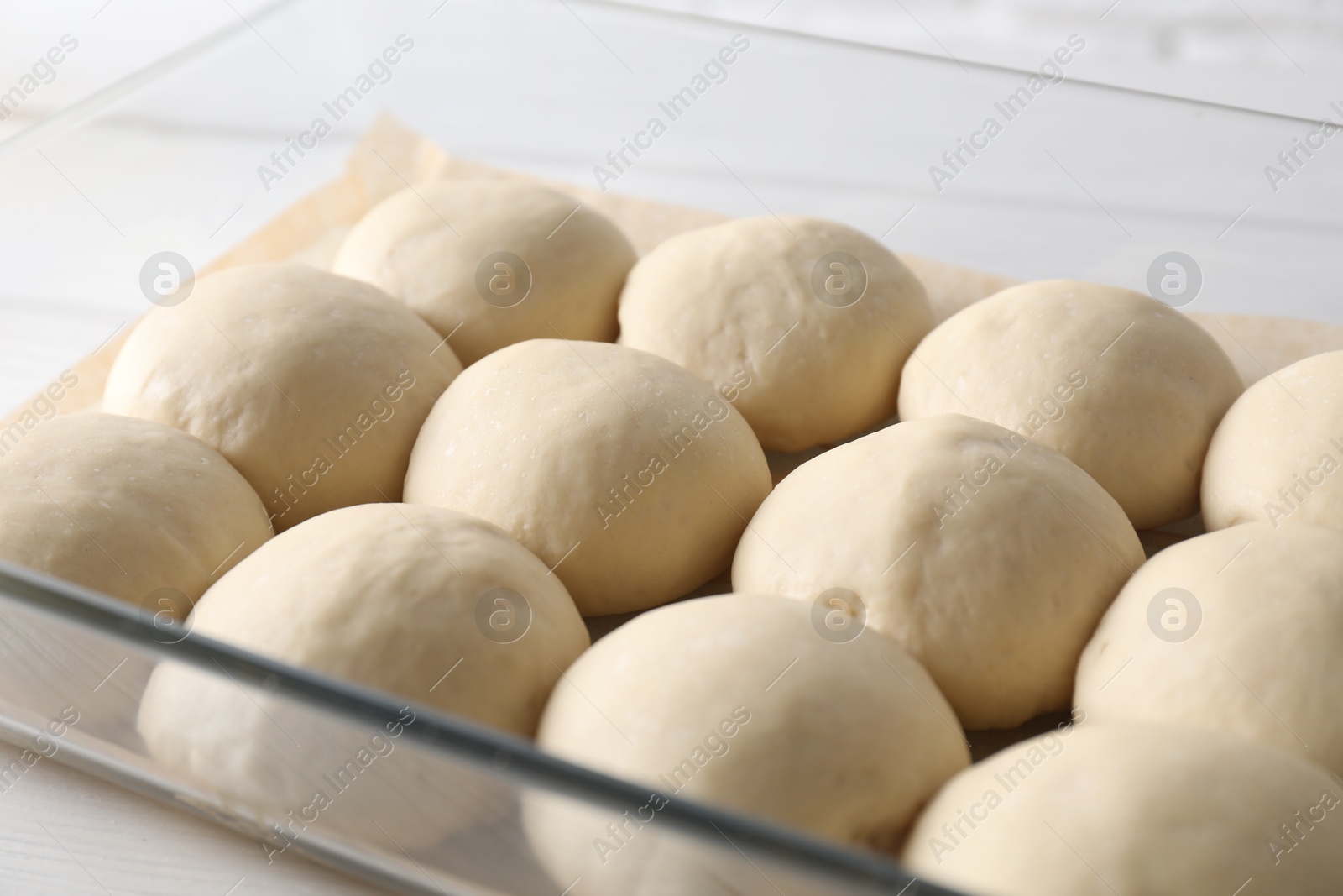 Photo of Raw dough balls in baking dish on table, closeup