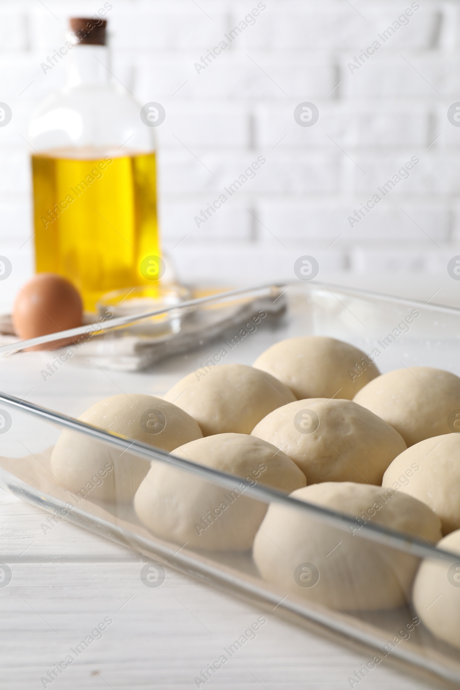 Photo of Raw dough balls in baking dish, egg and oil on white wooden table