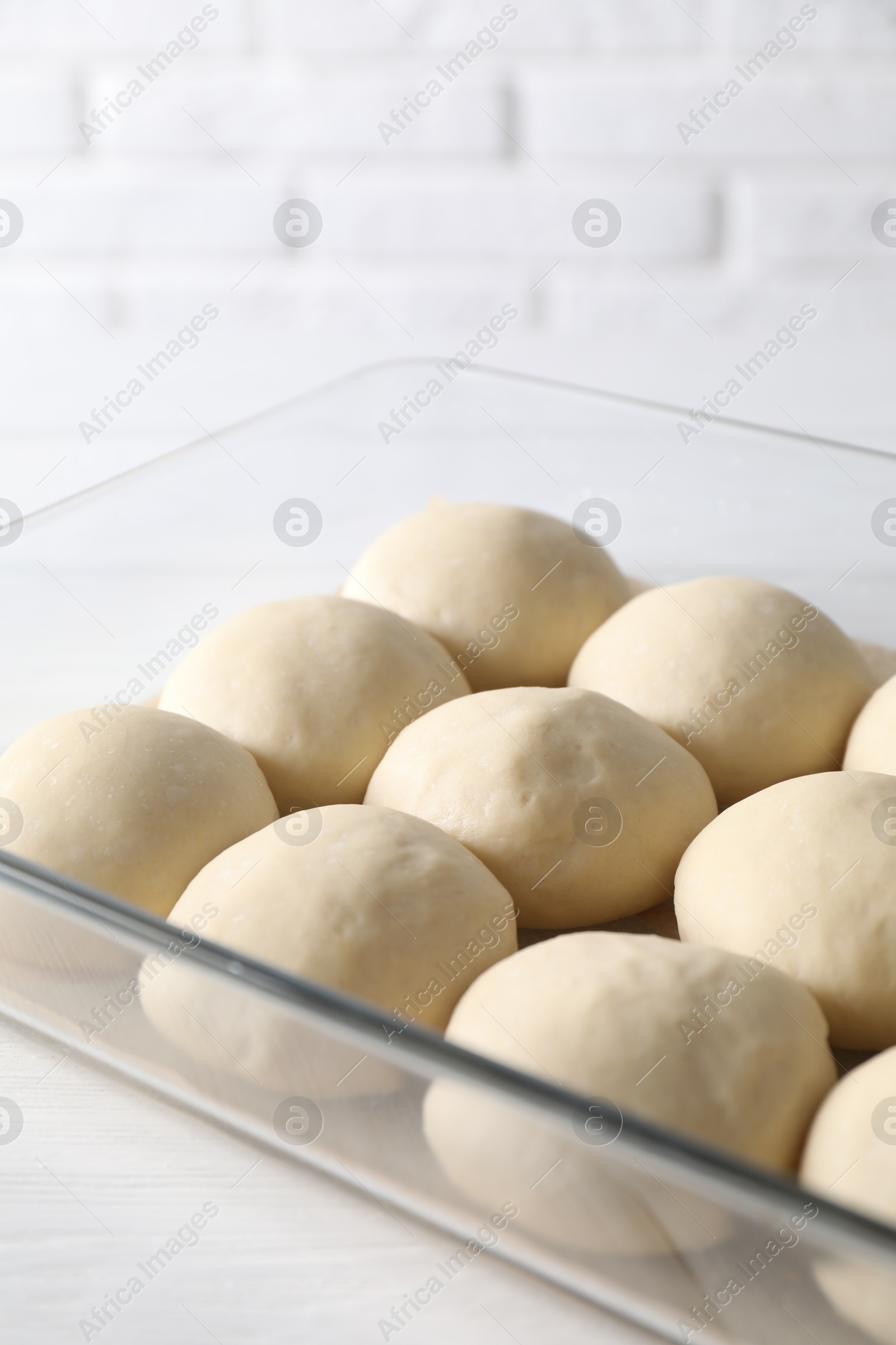 Photo of Raw dough balls in baking dish on white wooden table