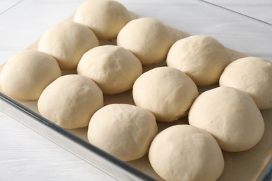 Raw dough balls in baking dish on white wooden table