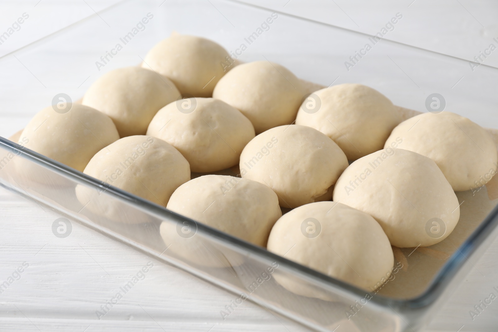 Photo of Raw dough balls in baking dish on white wooden table