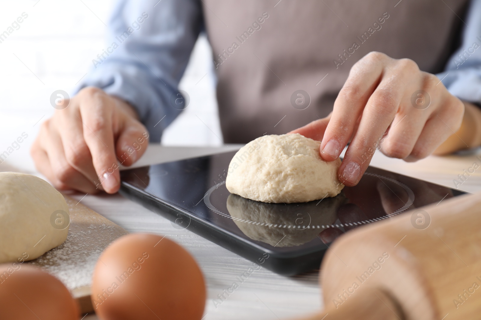 Photo of Woman weighing raw dough ball on kitchen scale at white wooden table, closeup