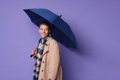 Young man with blue umbrella on purple background, space for text