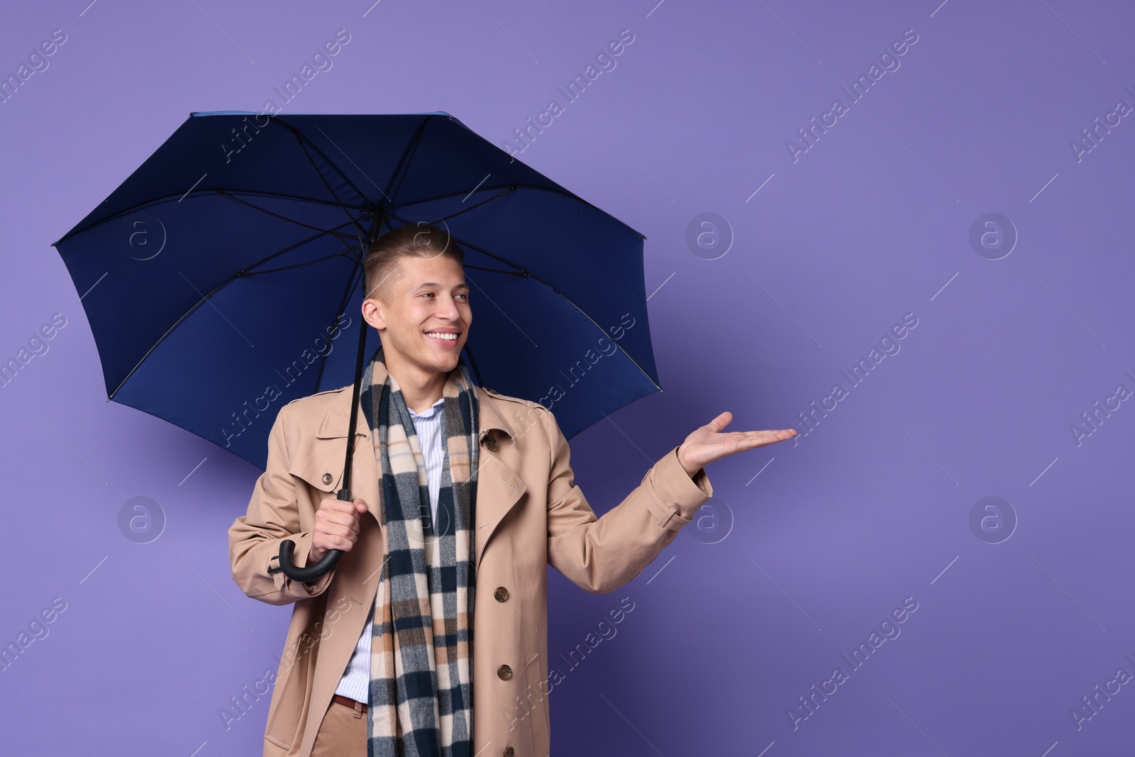 Photo of Young man with blue umbrella on purple background