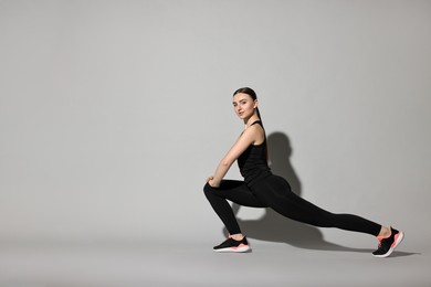 Aerobics. Young woman doing stretching exercise on light grey background. Space for text