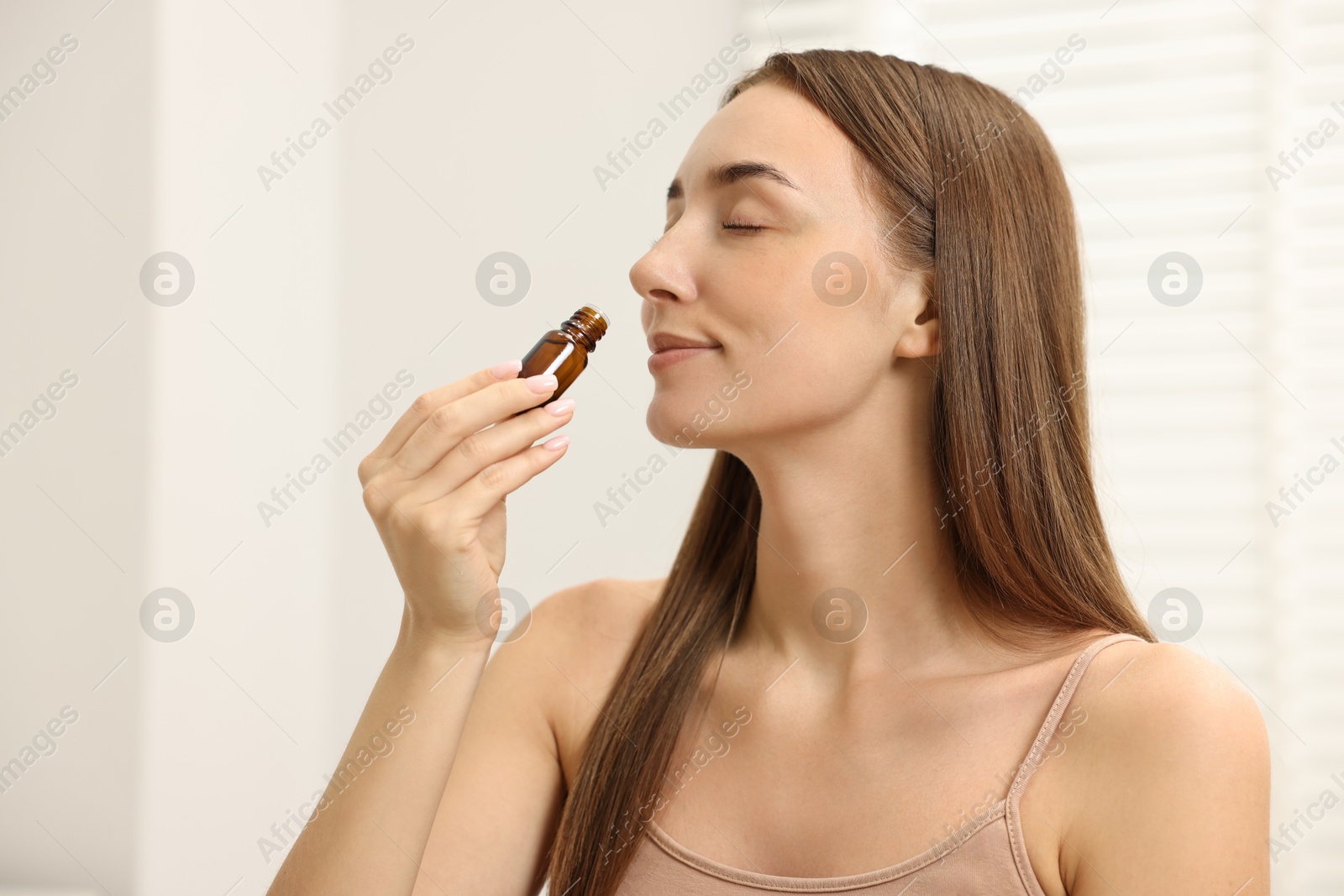 Photo of Aromatherapy. Beautiful woman with bottle of essential oil indoors