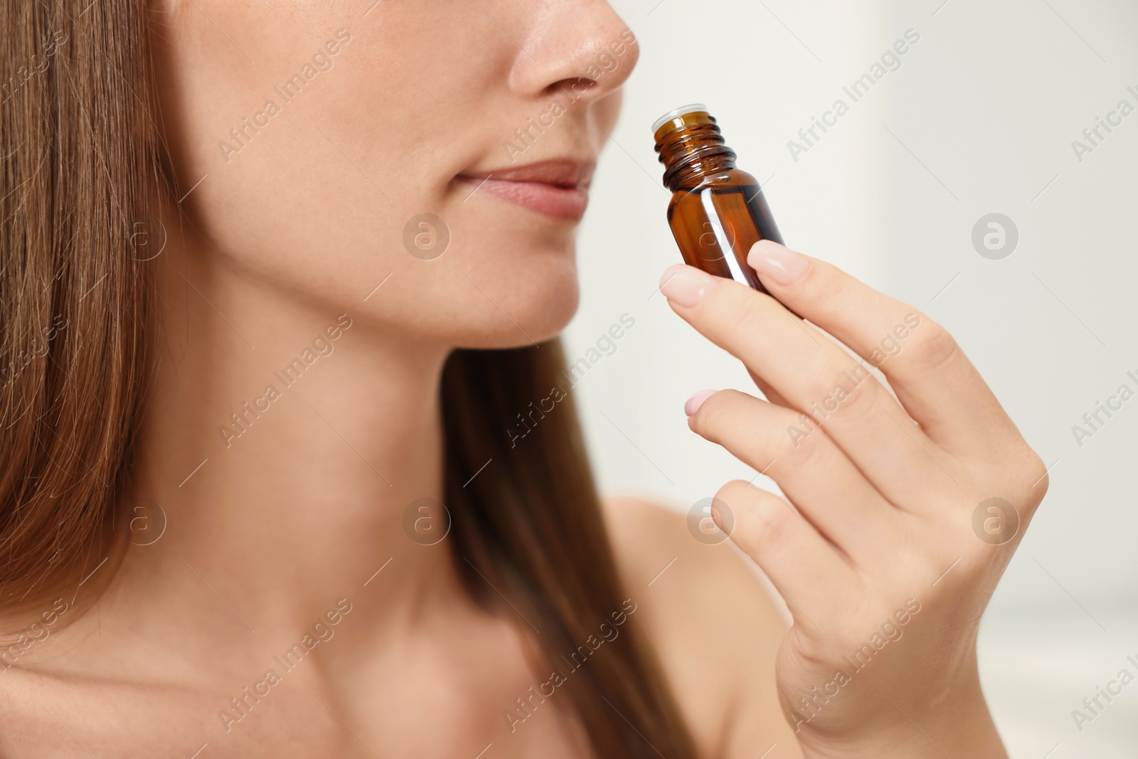 Photo of Aromatherapy. Woman with bottle of essential oil on light background, closeup