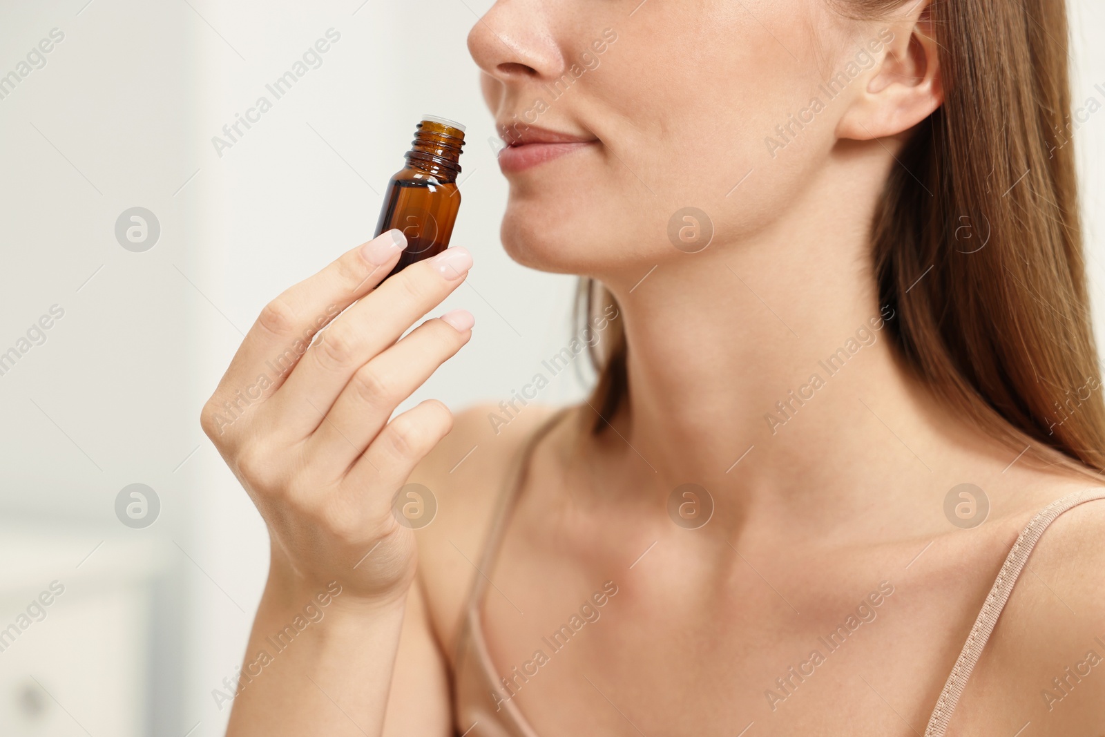 Photo of Aromatherapy. Woman with bottle of essential oil on light background, closeup