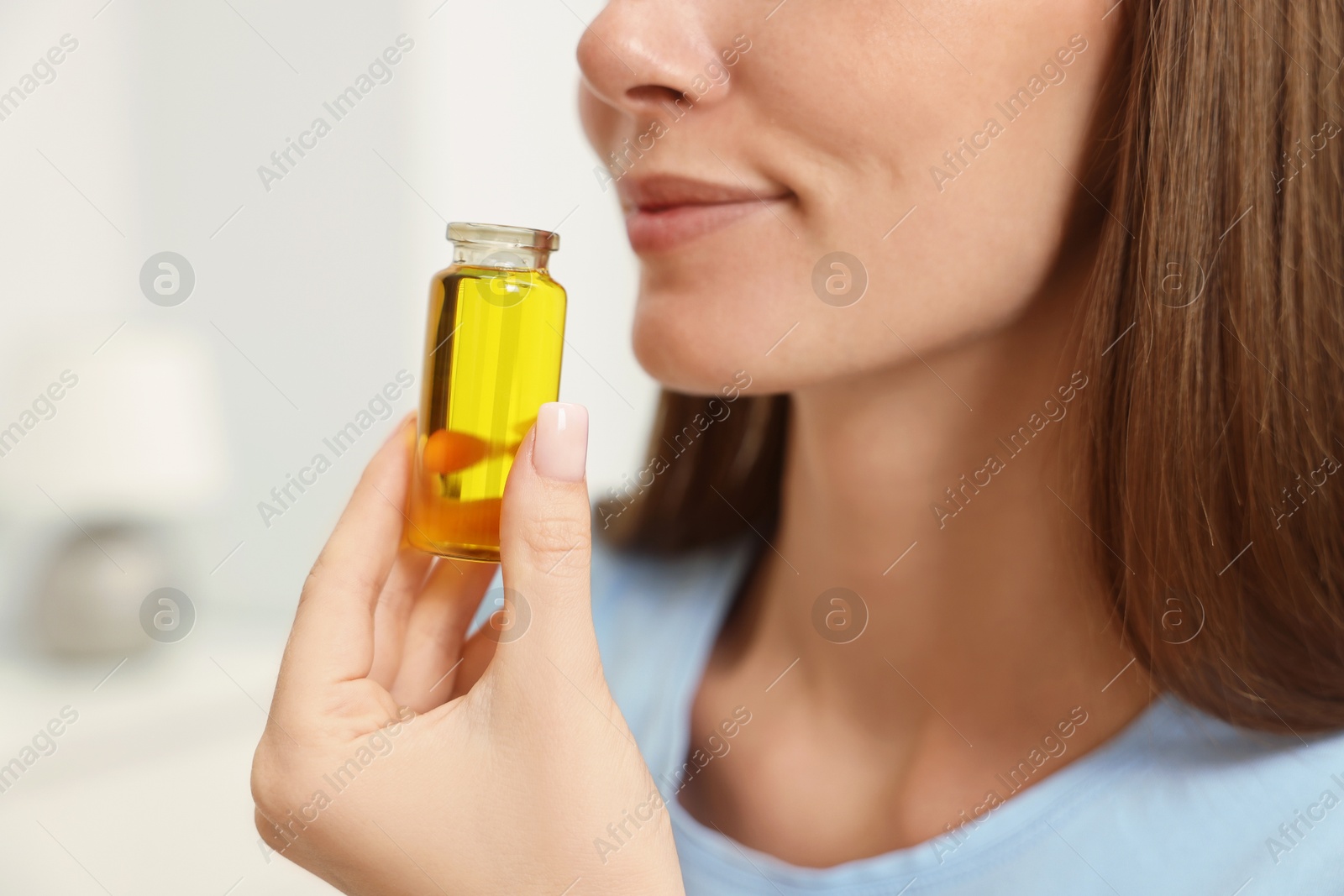 Photo of Aromatherapy. Woman with bottle of essential oil on light background, closeup