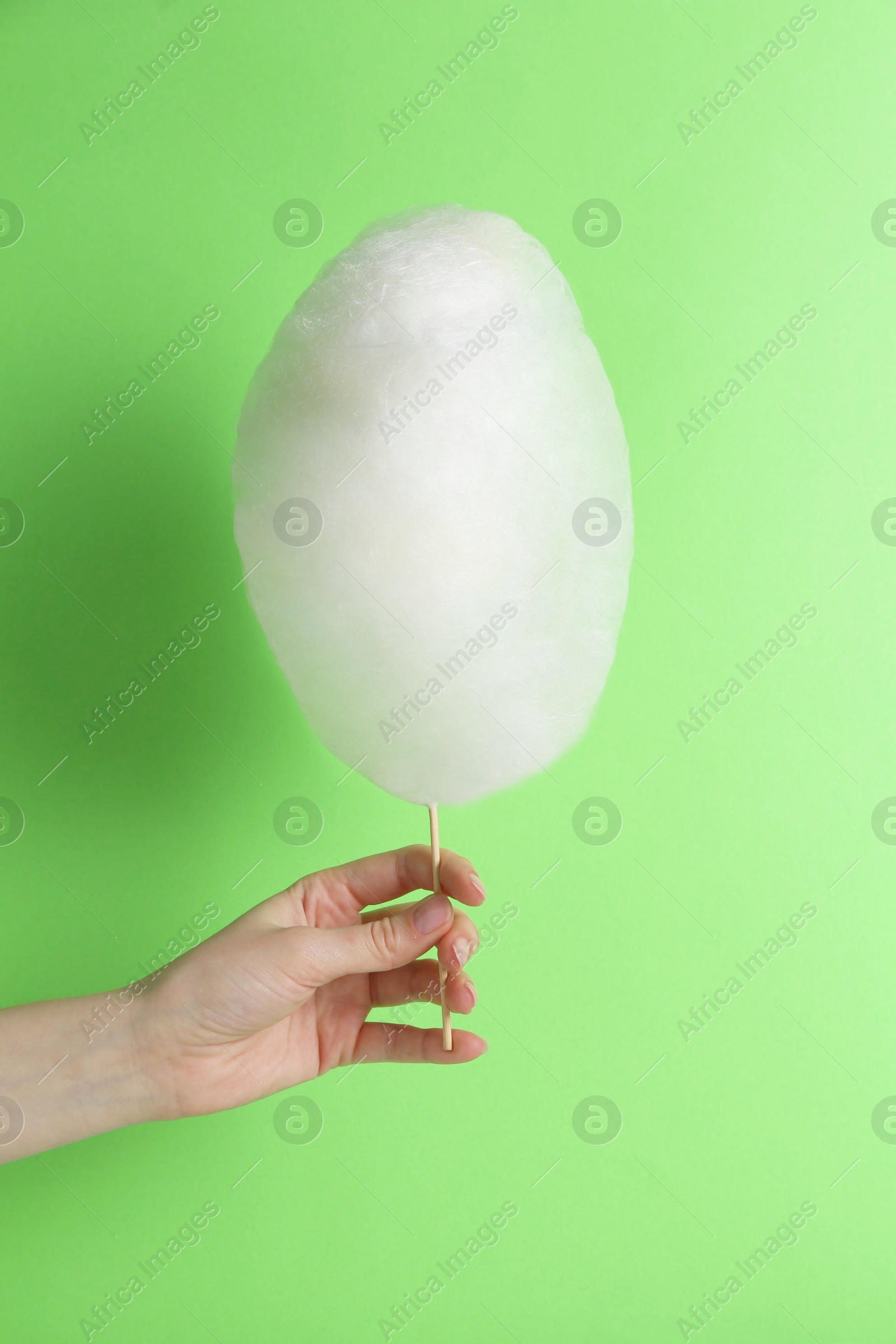 Photo of Woman holding sweet cotton candy on light green background, closeup