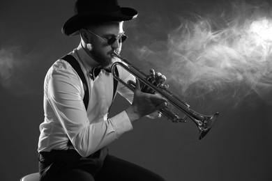 Photo of Professional musician playing trumpet on dark background with smoke, space for text. Black and white effect