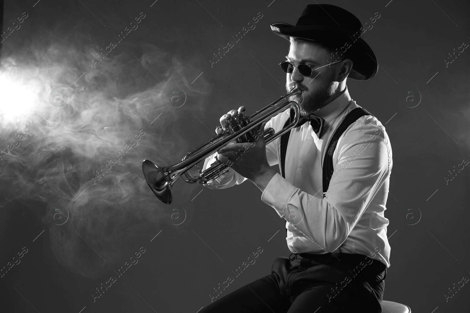 Photo of Professional musician playing trumpet on dark background with smoke, space for text. Black and white effect