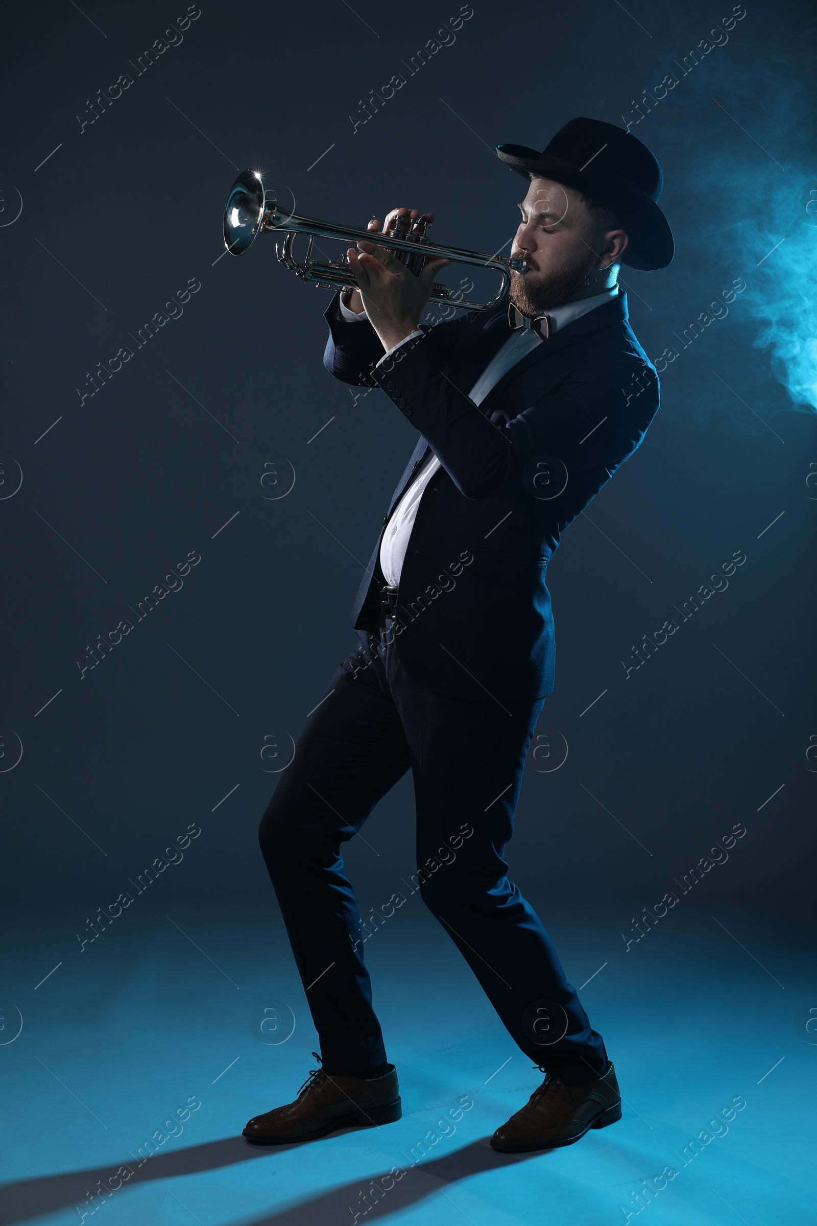 Photo of Professional musician playing trumpet on dark background in blue lights and smoke