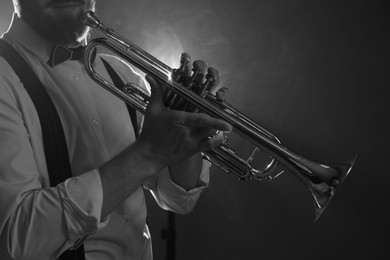 Professional musician holding trumpet on dark background, closeup with space for text. Black and white effect