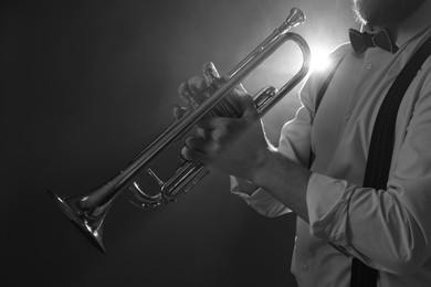 Professional musician holding trumpet on dark background, closeup with space for text. Black and white effect