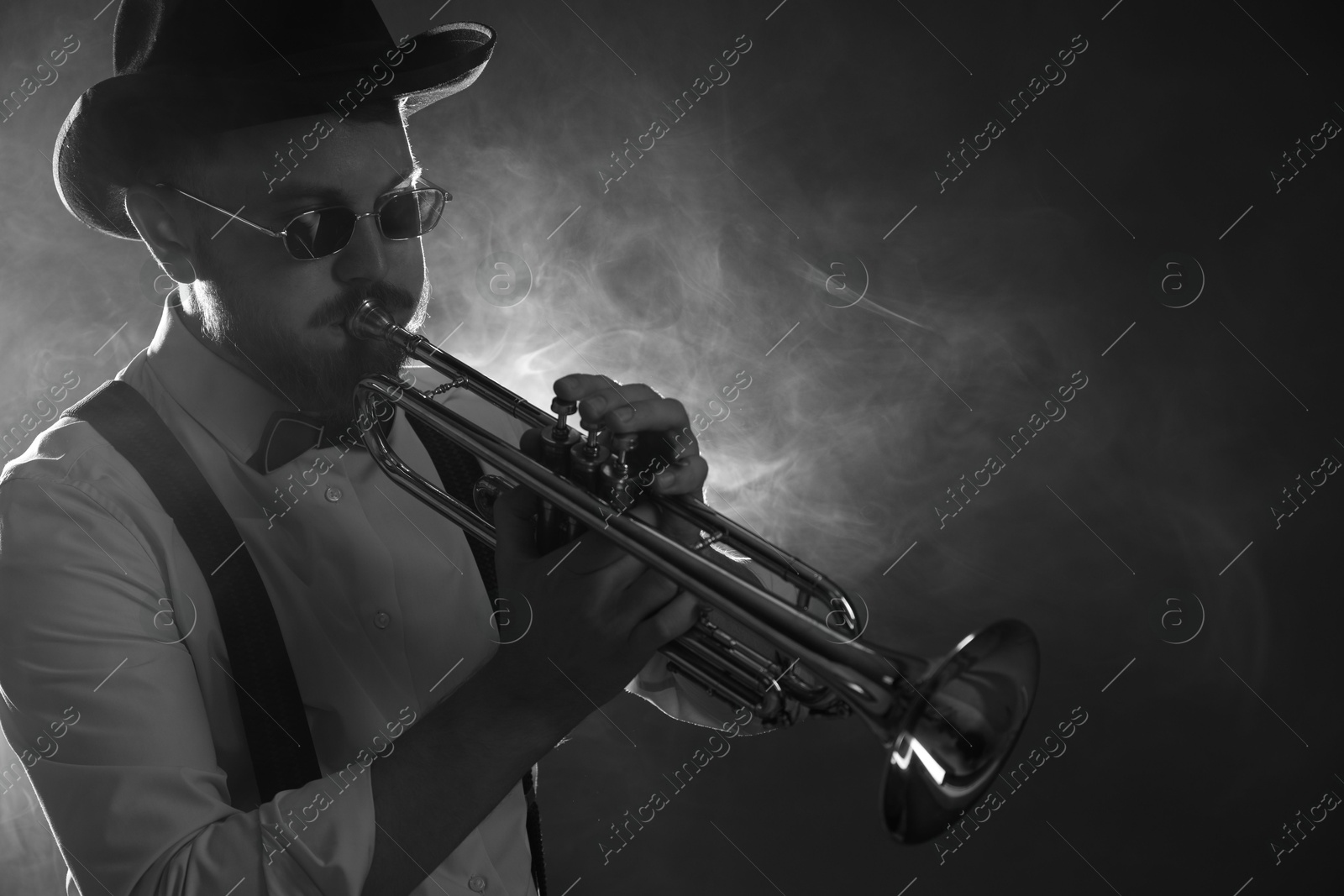 Photo of Professional musician playing trumpet on dark background with smoke, space for text. Black and white effect