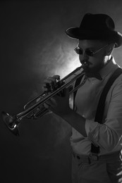 Photo of Professional musician playing trumpet on dark background with smoke. Black and white effect