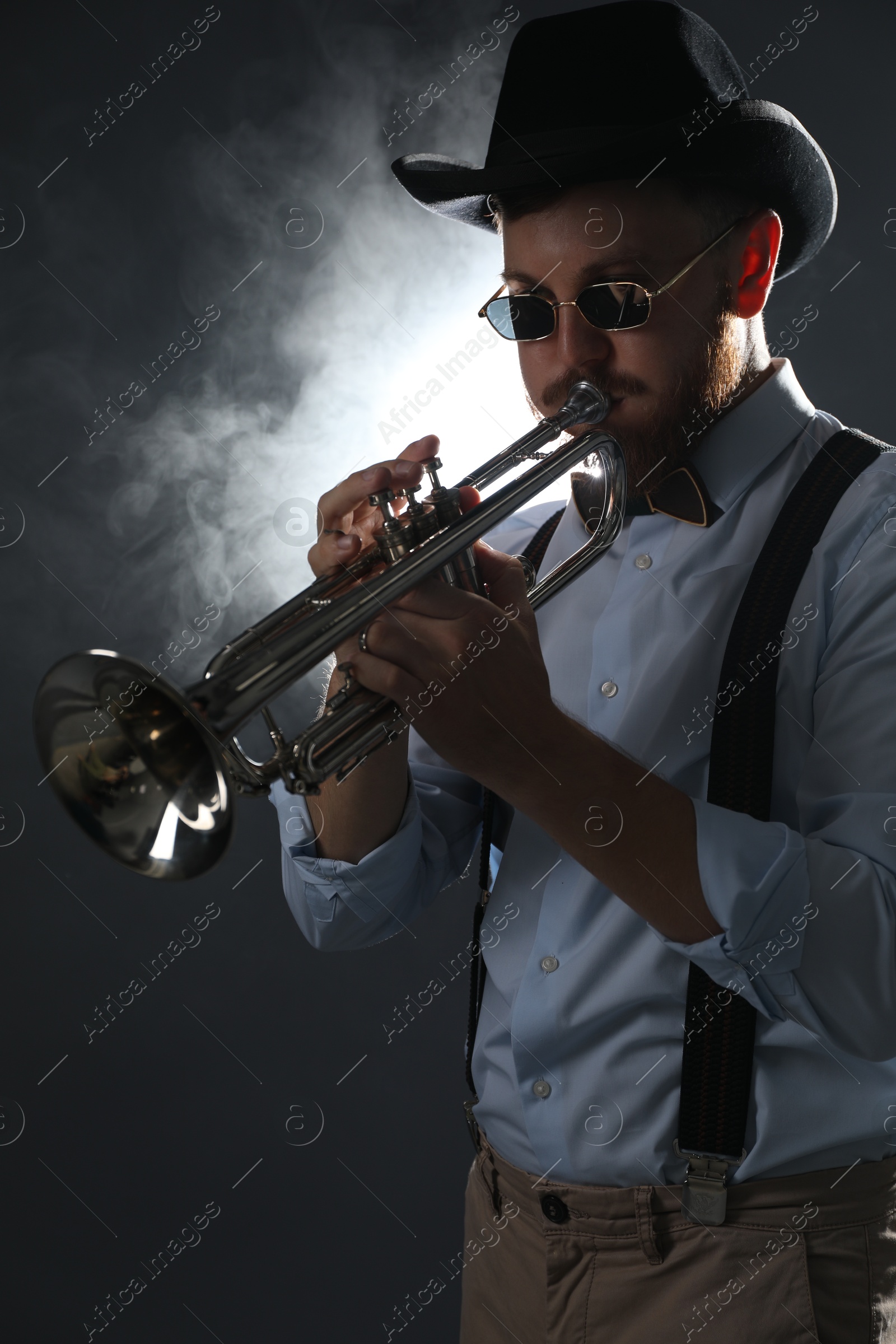 Photo of Professional musician playing trumpet on dark background with smoke