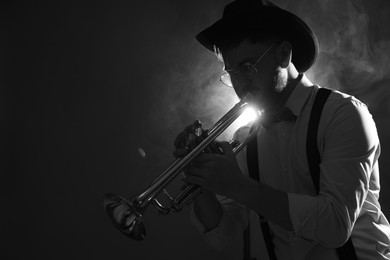 Professional musician playing trumpet on dark background with smoke, space for text. Black and white effect